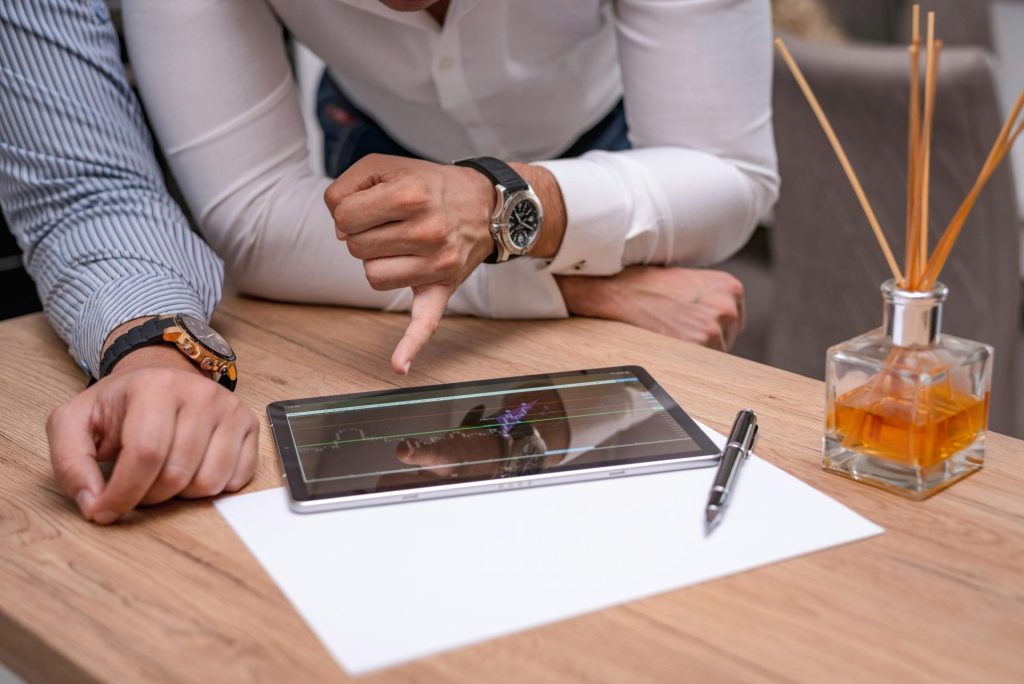 Zwei Geschäftsleute besprechen an einem Holztisch ein Diagramm auf einem Tablet.
